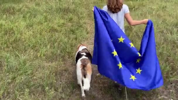 4k Маленькая девочка с большим флагом Европейского союза гуляет с собакой. Вид сзади. — стоковое видео