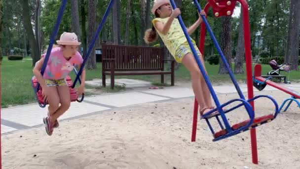 4k tweeling kleine meisjes swingen op een schommel op een speeltuin in een park. — Stockvideo
