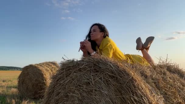 4k Thoughtful jovem mulher em vestido amarelo relaxante em uma pilha de palha. — Vídeo de Stock