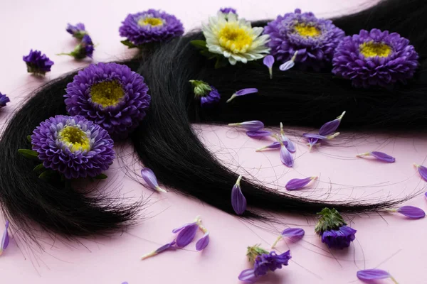 Cabelo escuro com flores lilás e pétalas. Conceito de cuidados capilares. — Fotografia de Stock