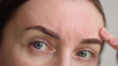 Kalıcı makyajdan sonra iyileşen kaşlarına bakan bir kadın. - Yakın çekim. 4k görüntü