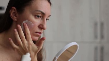Aynanın önündeki kadın yüzüne krem maske takıyor. 4k görüntü