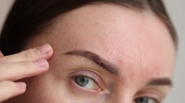 Kalıcı makyajdan sonra iyileşen kaşlarına bakan bir kadın. - Yakın çekim. 4k görüntü