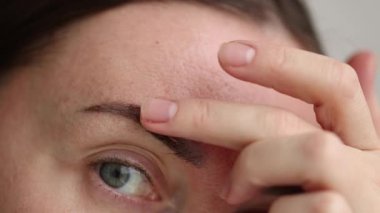 Woman wants to take off piece of dry skin from eyebrow after permanent makeup. Closeup. 4K footage