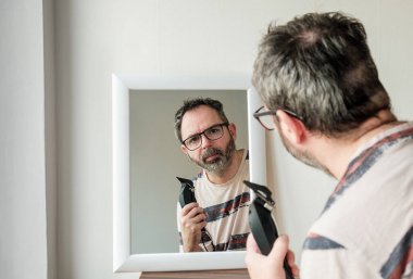 Elinde makasla aynaya bakan olgun bir adam..