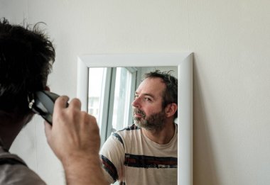 Yetişkin bir adam bazı zorluklarla kendi gri saçlarını kesiyor. Salgın izolasyonu.