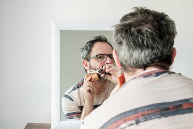 Olgun bir adam salgın sırasında kendi gri sakalını kesiyor..