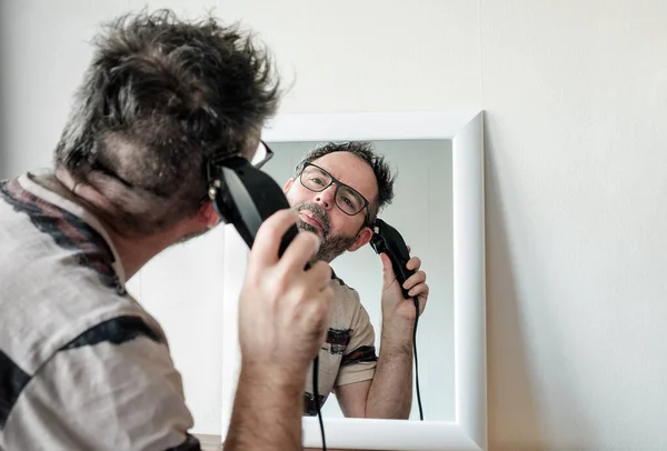 Olgun bir adam kendi gri saçını makasla kesiyor. Gözlük takıyor. Salgın.