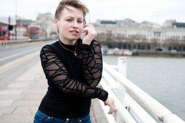 Rüzgarlı bir günde Londra Waterloo Köprüsü 'nde poz veren güzel genç bir kadın..