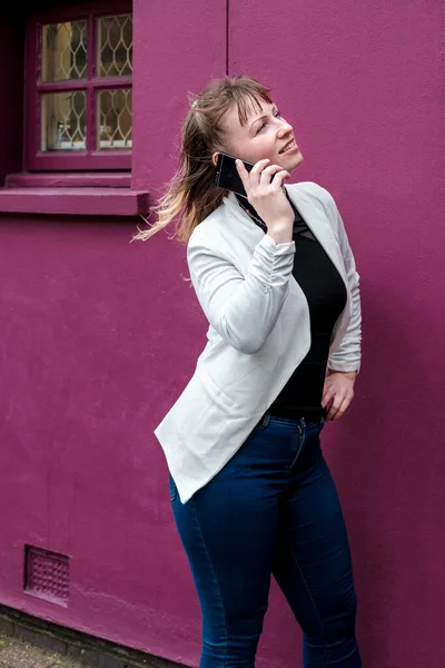 Молодая Блондинка Идет Рядом Фиолетовой Стеной Используя Свой Телефон — стоковое фото