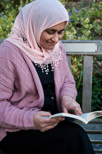 Mature muslim woman wearing hijab is reading a book in a park.