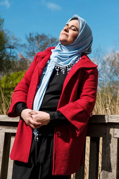 Başörtüsü takan Müslüman kadın tırabzana yaslanıyor. Sabahları güneşin tadını çıkarıyor..