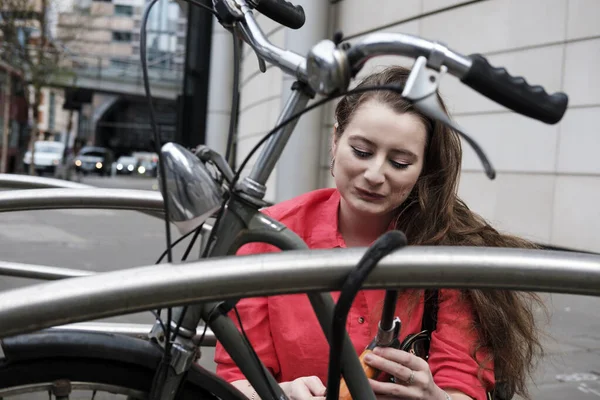 Kırmızı tişörtlü genç bir kadın bisikletinin kilidini açıyor. Londra caddesinde bisiklet kilitlenmesi.