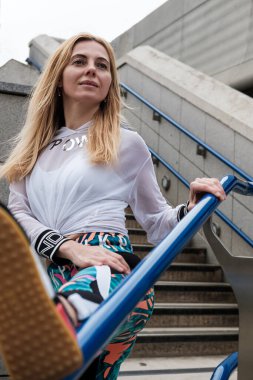 Çekici olgun bir kadının portresi. Açık bir tırabzanda bacağını esnetiyor..