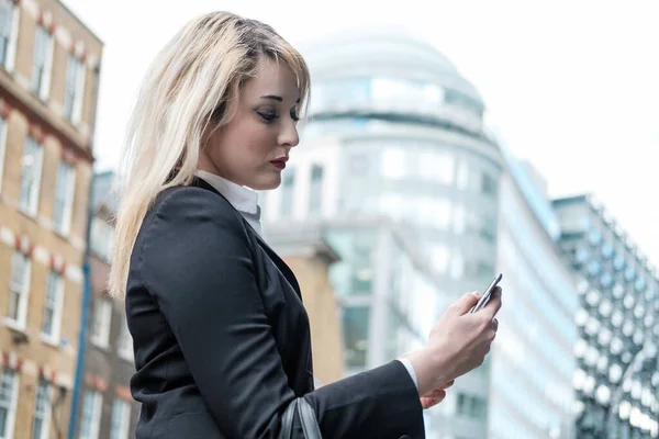 Stylist young business woman using smartphone in the street. Wearing suit jacket.