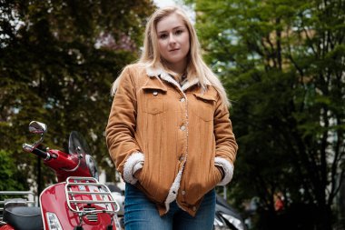 Şehir ortamında arkasında scooterlarla poz veren genç sarışın kadın portresi..