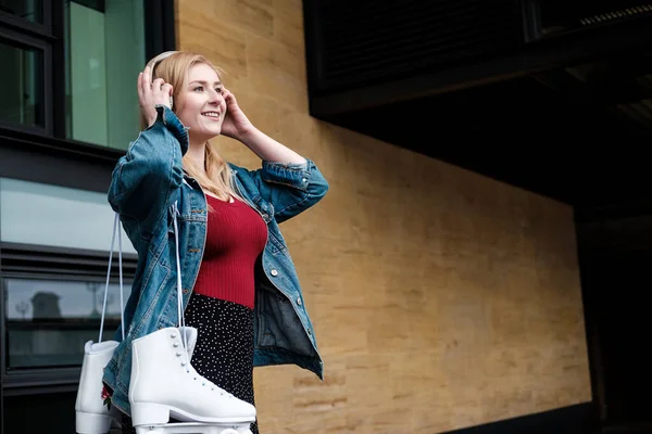 Mujer Joven Usando Auriculares Está Pie Sosteniendo Patines Ella Sonríe —  Fotos de Stock