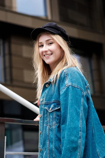 Arkasında tırabzan olan genç bir kadının portresi. O kot ceket giyiyor. Gülümsüyor.