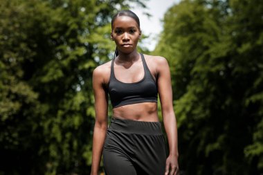 Siyah genç bir kadın parkta egzersiz yapıyor. Kameraya doğru emin adımlarla yürüyor..