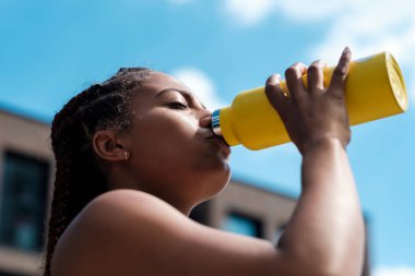 Sarı şişeden içen çekici genç bir kadın. Sıcak yaz günü. Karışık ırk.