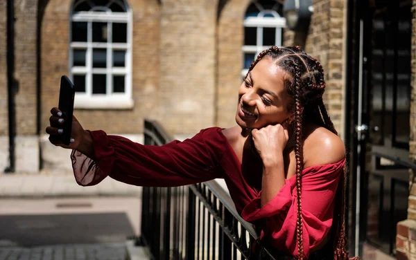 Akıllı telefonlu genç bir kadın sıcak bir yaz gününde Londra sokaklarında selfie çekiyor..