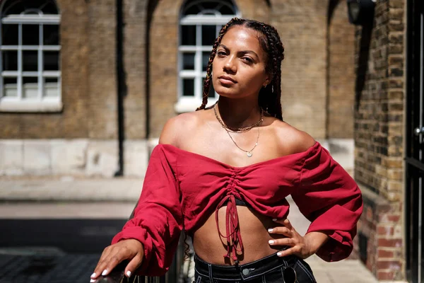 Sıcak bir yaz gününde Londra sokaklarında poz veren havalı saçlı genç bir kadın. Örgülü ve kırmızı bluz giyiyor..