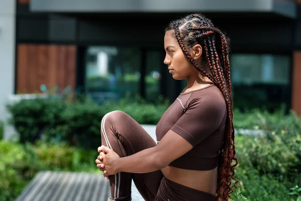 Spor kıyafetleri giyen ve şehir ortamında poz veren genç bir kadın. Karışık ırk, örgü..