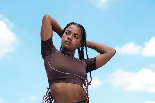 Spor giyinen ve esneme hareketleri yapan genç bir kadın. Mavi gökyüzü. Karışık ırk, örgü..