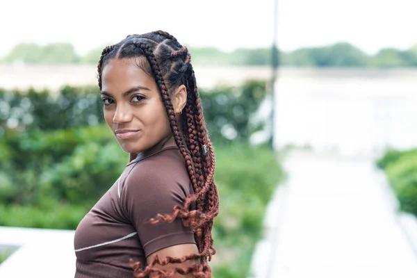 Kameraya bakan genç bir kadının portresi. Braid, melez ırk. Spor kıyafetleri giyiyor..