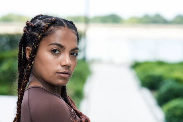 Kameraya bakan genç bir kadının doğal portresi. Braid, melez ırk. Spor kıyafetleri giyiyor..