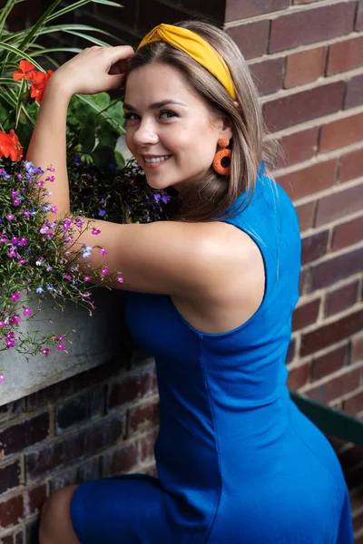 Çiçeklere yakın poz veren çekici genç bir kadının portresi. Güneşli bir yaz gününde mavi bir bahar elbisesi giyiyor..