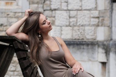 Kilisenin önündeki bankta oturan genç bir kadın. O şık kahverengi bir elbise giyiyor..