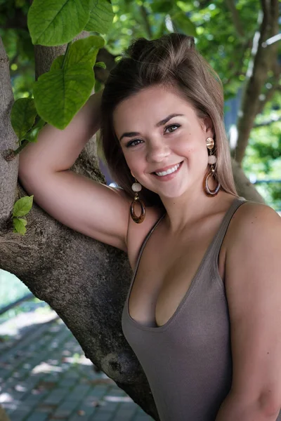 Çekici bir genç kadının portresi ağaca yaslanmış duruyor. O şık kahverengi bir elbise giyiyor..