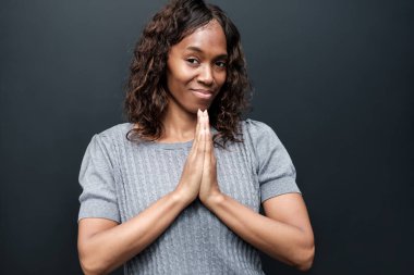 Dünya sağır günü. Olgun siyah sağır kadın siyah arka planda işaret dili kullanıyor. Gülümsüyor ve gri bir tişört giyiyor..