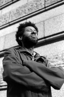 Afro saçlı, çapraz kollu, taş bir duvara karşı derin derin derin meditasyon yapan, tek renkli analog antika efektli, görünür tahıllı, 35 mm 'lik filmle çekilen Afro Amerikalı genç bir adam.