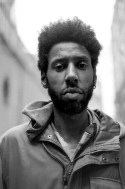 Afro saçlı, sıradan kıyafetler giyen, şehir ortamında duran, klasik 35 mm 'lik film estetiğiyle yakalanmış Afro-Amerikan bir adamın tek renkli portresi.