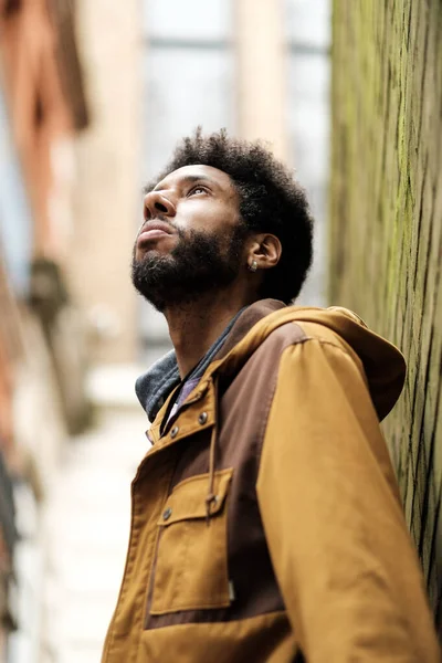 Şık sakallı, afro saçlı, modaya uygun kahverengi ceketli ve küpeli dar bir şehir sokağında özenle dik dik bakan genç bir zenci portresi.