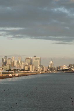 Kanarya Rıhtımı nehir üzerinde yükseliyor. Londra şehri havaalanı pisti altın saat ön planda. Günbatımında modern finans ve deniz kenarı yaşamını yansıtıyor.