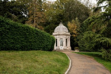 Etrafı manikürlü çitlerle, yeşil otlarla çevrili dolambaçlı bir çakıl yolunun sonunda duran, kubbeli bir çatısı olan süslemeli klasik taş çardağı ve huzurlu bir park ortamında yemyeşil ağaçlar.