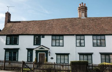 Beyaz boyalı tarihi İngiliz kulübesi yeşil çerçeveli pencereler, ahşap ön kapı ve terasotta kaplama çatı birden fazla baca, klasik köy cazibesi