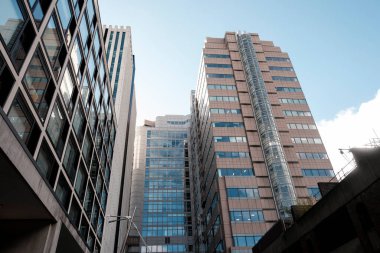 Modern şehir gökdelenleri, şehir ortamını ve mavi gökyüzünü etkileyici cam cephelerine yansıtarak çağdaş mimarinin dinamik bir görüntüsünü yaratırlar.