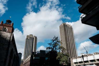 Barbika merkez kulelerinin acımasız mimarisi beyaz bulutlu mavi gökyüzüne karşı dimdik ayakta duruyor, Londra 'daki antik tuğla kilise kulesiyle çelişiyor.