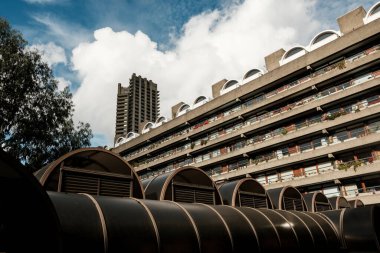 Barbican malikanesi bulutlu bir gökyüzünün altında belirgin beton cephelerini, balkonlarını ve kemerli camlarını gösteriyor. Bu Londra 'da kentsel yaşam için barbar mimarinin önemli bir örneğini temsil ediyor.