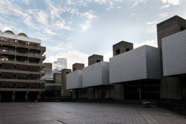 Barbika merkez kompleksi, zıt mimari tarzları beton yapılar ve tekrarlayan kare formlarla göstererek, bulutlu bir gökyüzü altında kentsel bir zemin sağlıyor