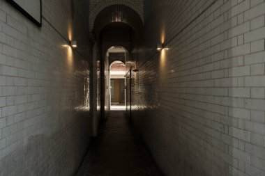 Duvarları kiremitli, uzun, karanlık bir koridor. Duvarın ışıklarıyla aydınlatılıyor. Ilık ışık yansıtıyor ve yansımalar yaratıyor.