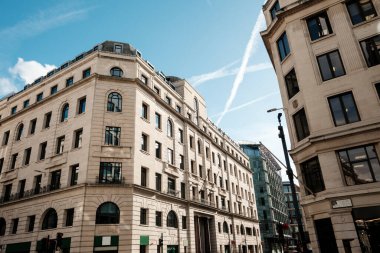 Bir sokak köşesini tanımlayan şehir mimarisi, klasik cepheleri ve modern unsurları beyaz zıtlıklarla bembeyaz gökyüzüne karşı sergiliyor, iş ve şehir yaşamını temsil ediyor.