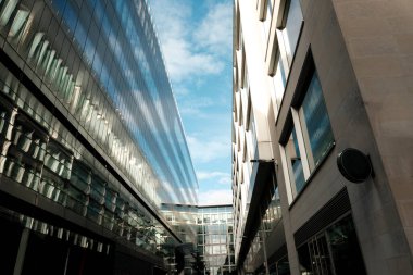 Çağdaş mimari tarzları ve mavi gökyüzünün bulutlu yansımalarını gösteren yansıtıcı cam cepheleri ve beton bir yapıya sahip modern kentsel binalar