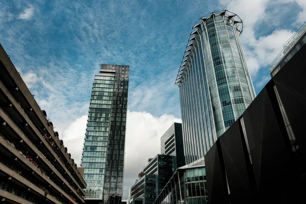 Londra Barbika bölgesi farklı mimari tarzlar sergiliyor. Beton, mavi gökyüzü ve bulutlar altında yükselen gökdelenler.