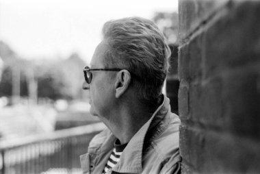 Düşünceli, gözlüklü, tuğla bir duvarın yanında duran ve bakışlarını kaçıran, nostaljik bir atmosferi çağrıştıran 35 mm 'lik eski bir kamerayla çekilmiş tek renkli, analog bir film portresi.