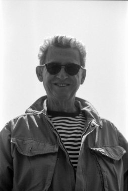 Güneş gözlüğü takan ve ceketinin altında çizgili gömlek giyen gülümseyen bir adamın tek renkli, analog film portresi. 35mm 'lik eski bir kamera ile yakalanmış. Zamansız ve nostaljik bir his yaratmak